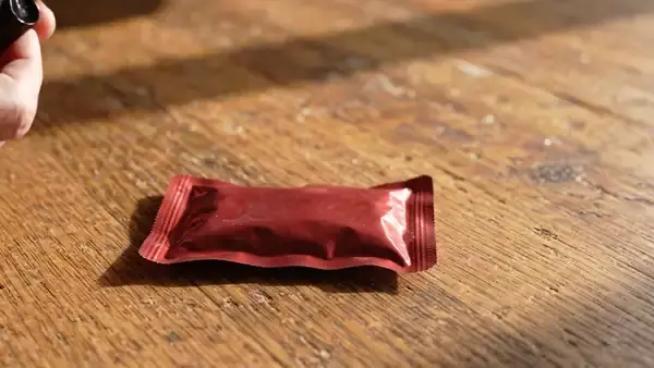 A black marker drawing a short tally line on the plain back of a small dark-red pouch